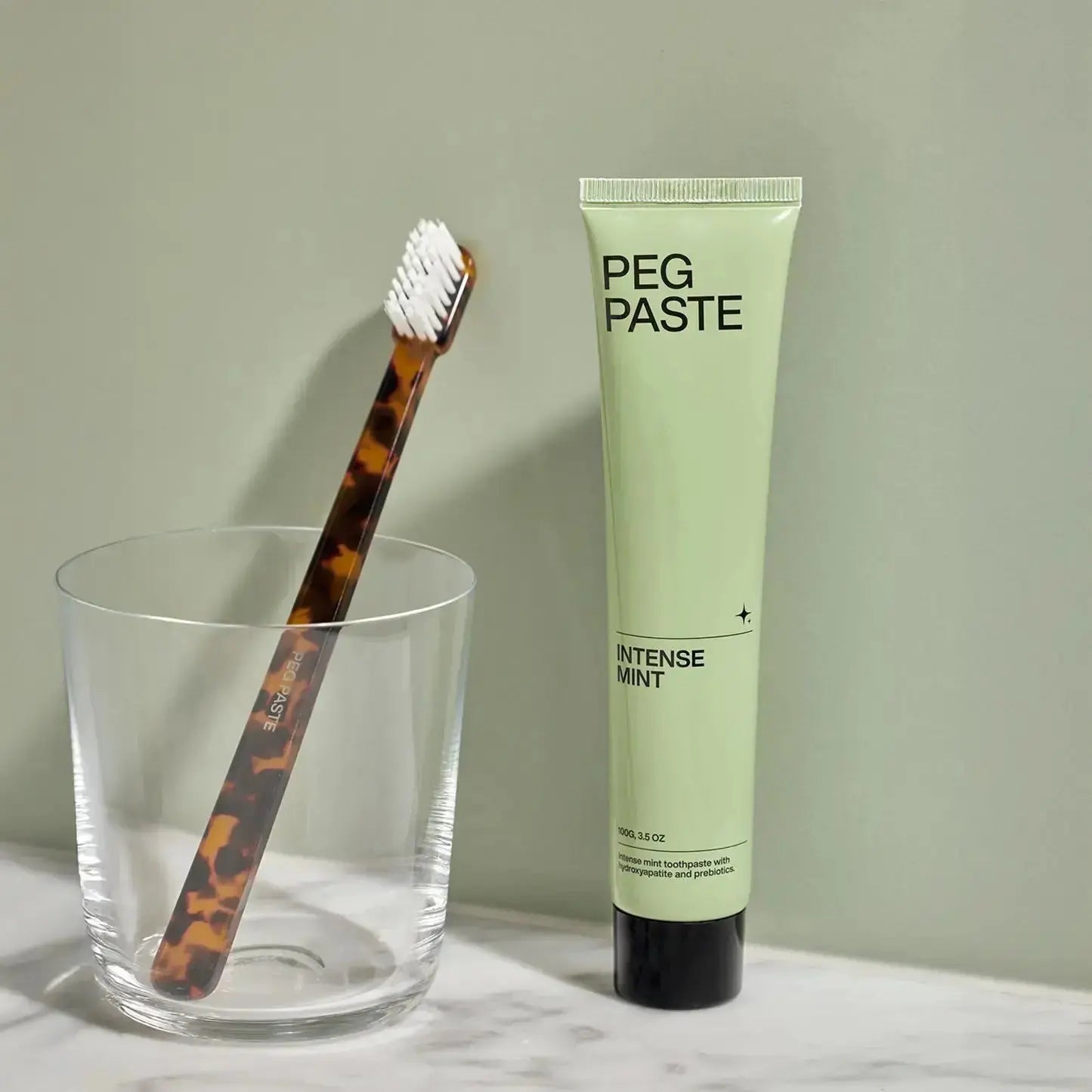 Peg Paste Intense Mint toothpaste beside a toothbrush in a travel bathroom setup