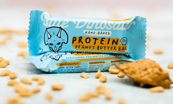 Blue Dinosaur Peanut Butter Protein Bar in turquoise wrapper surrounded by peanuts